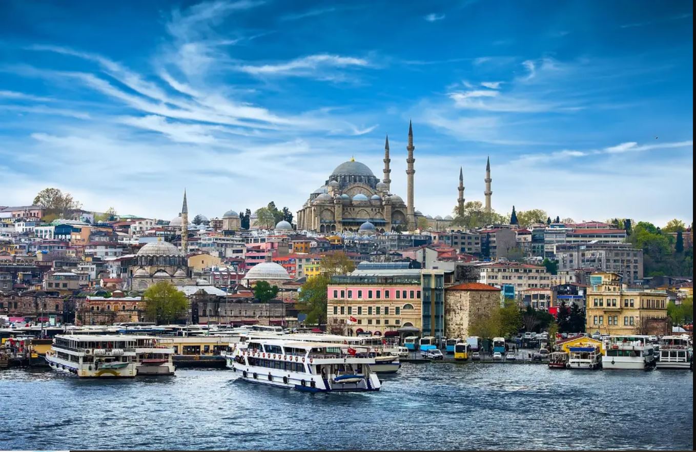 A scenic view of Istanbul’s waterfront featuring boats, colourful buildings, and the prominent Suleymaniye Mosque under a blue sky—perfect for those exploring the city with exclusive Holiday Packages.